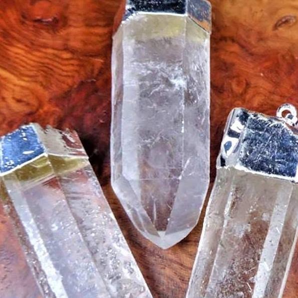 Three clear quartz crystal point pendants with silver-colored caps on a wooden surface