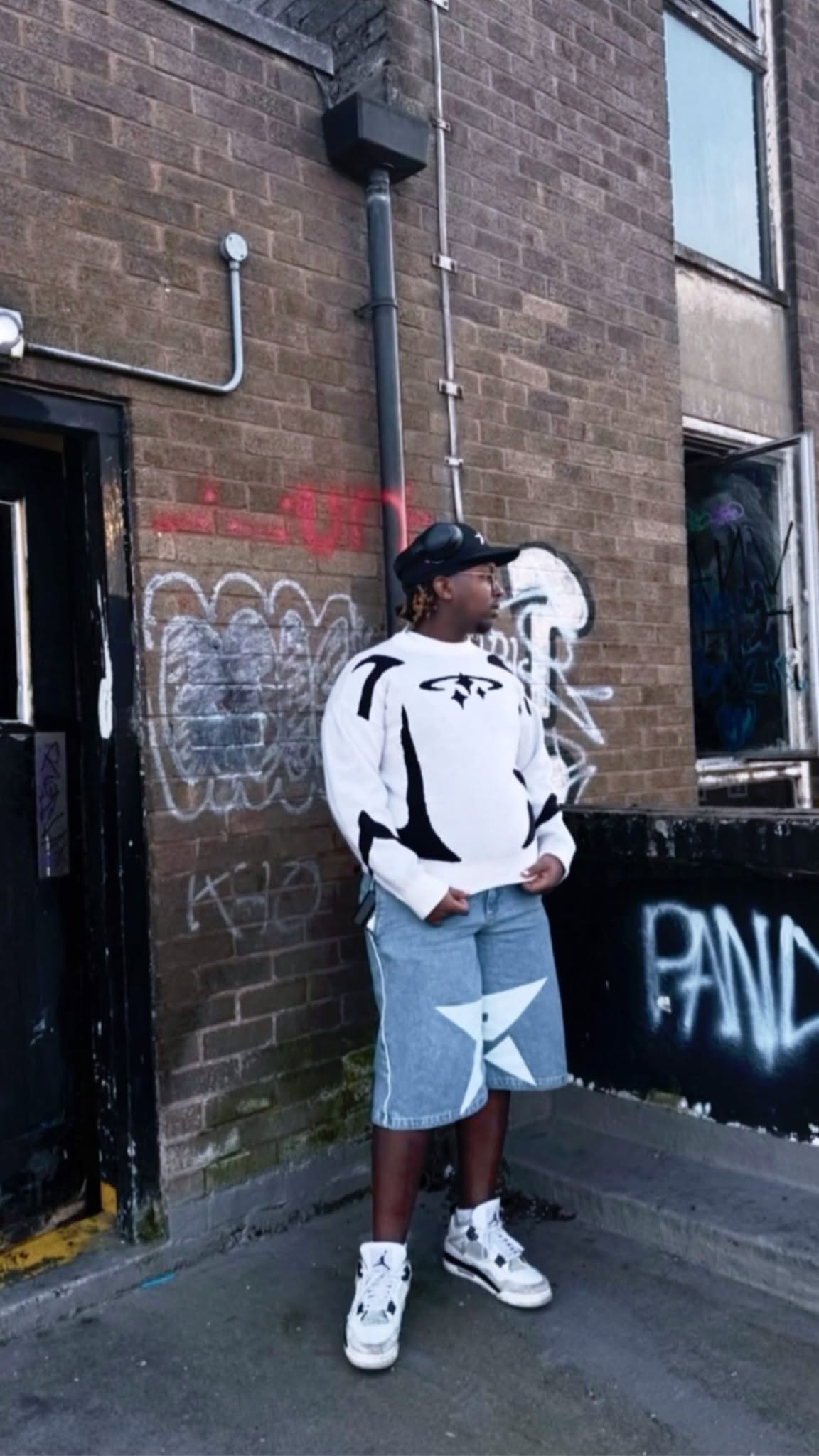 Man wearing a DCRB graphic knit sweater and denim shorts on a city street