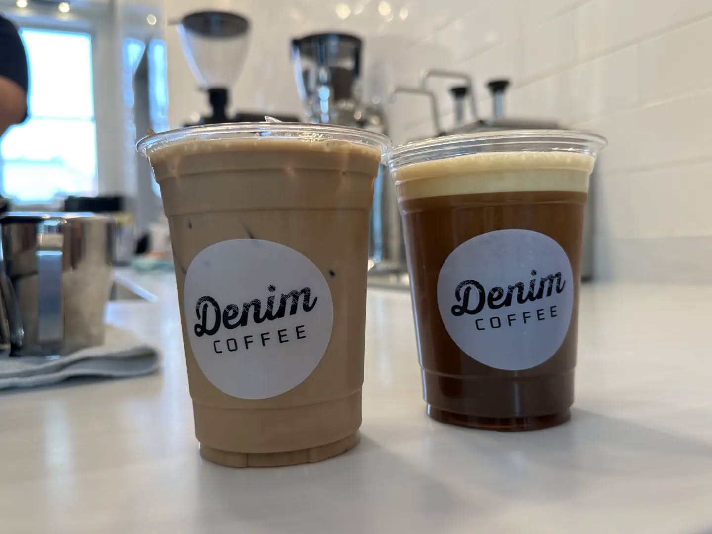 Two Denim Coffee branded iced coffee cups on a cafe counter