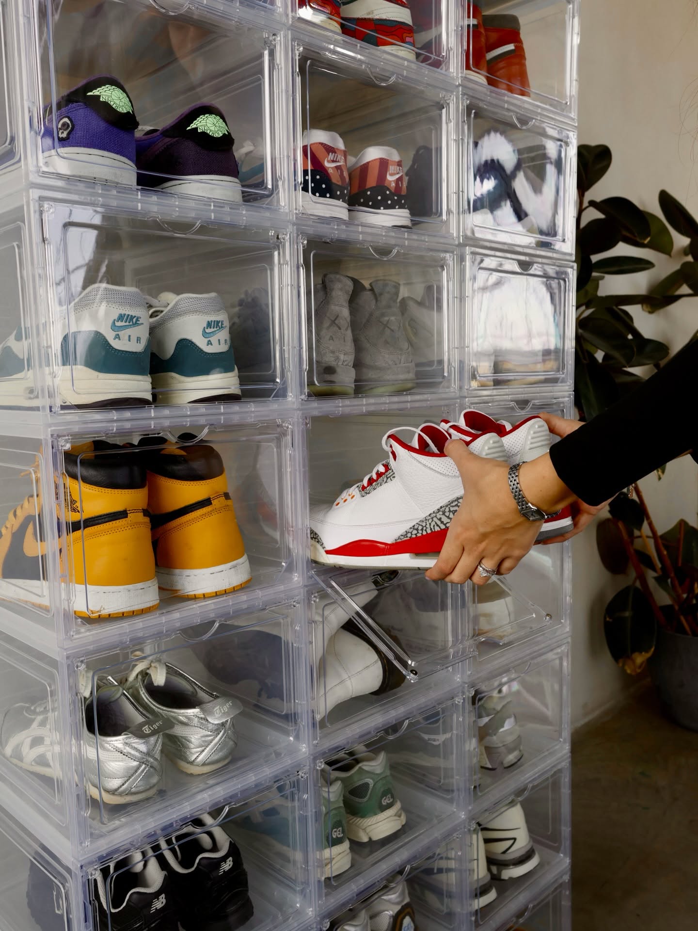 A hand pulling a pair of red and white sneakers out of a KicksBox acrylic storage box