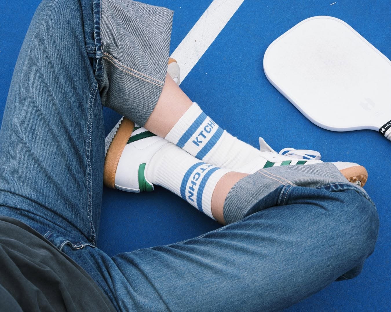 KTCHN striped crew socks worn with sneakers on a blue pickleball court