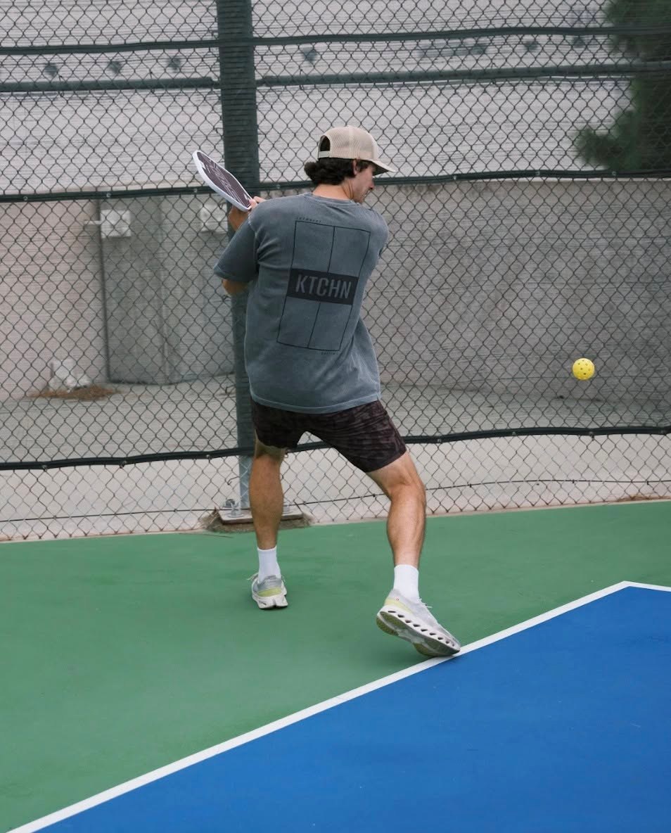 Player mid-swing in a KTCHN court-graphic tee