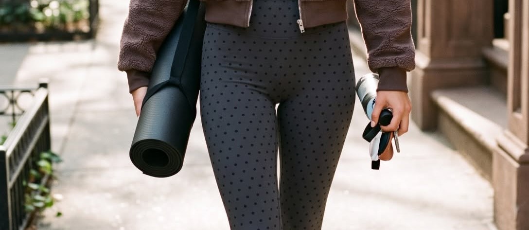 Woman walking a city street wearing Priv Form polka-dot leggings and carrying a yoga mat