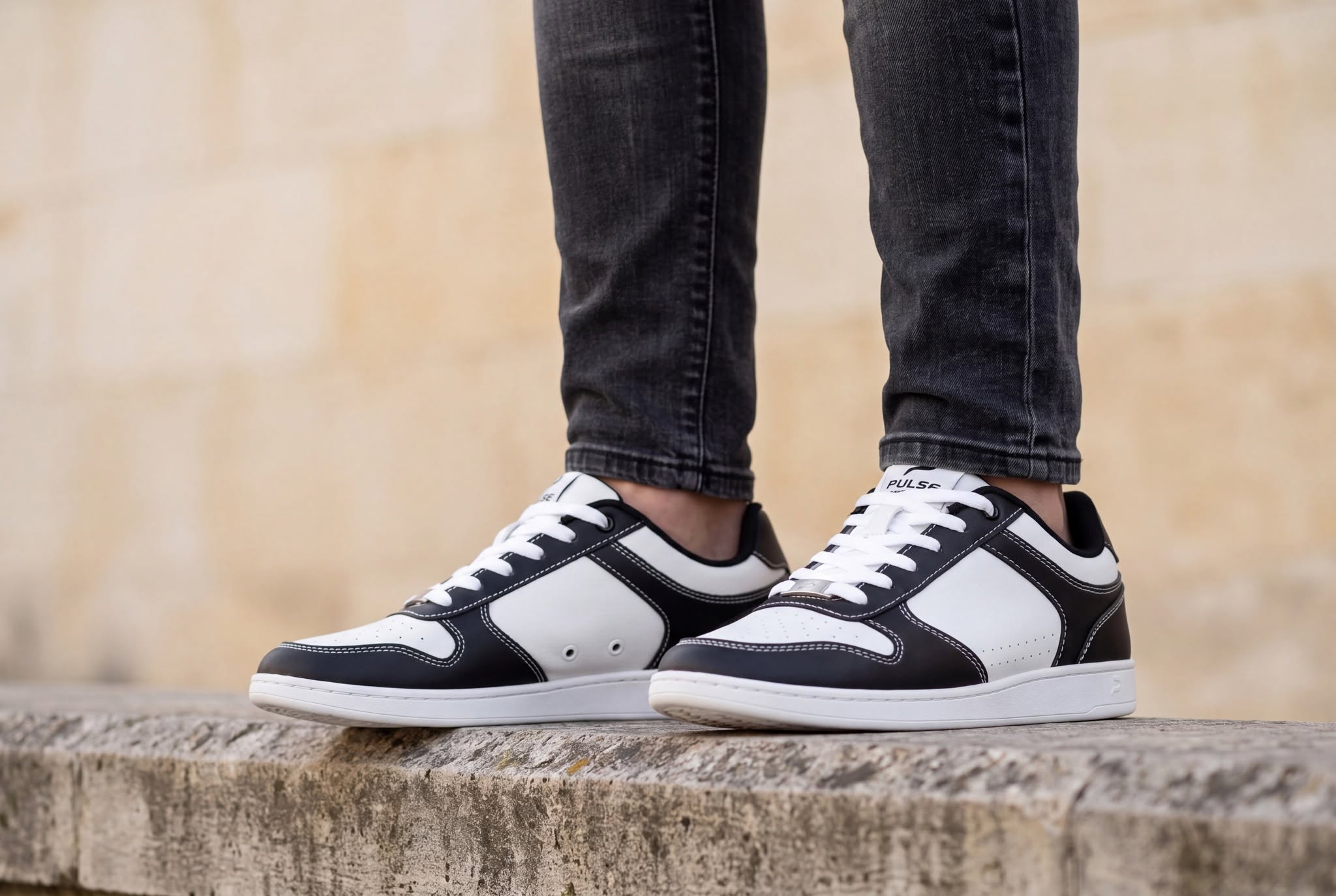 Black and white Pulse low-top dance sneakers worn with dark jeans on a stone ledge
